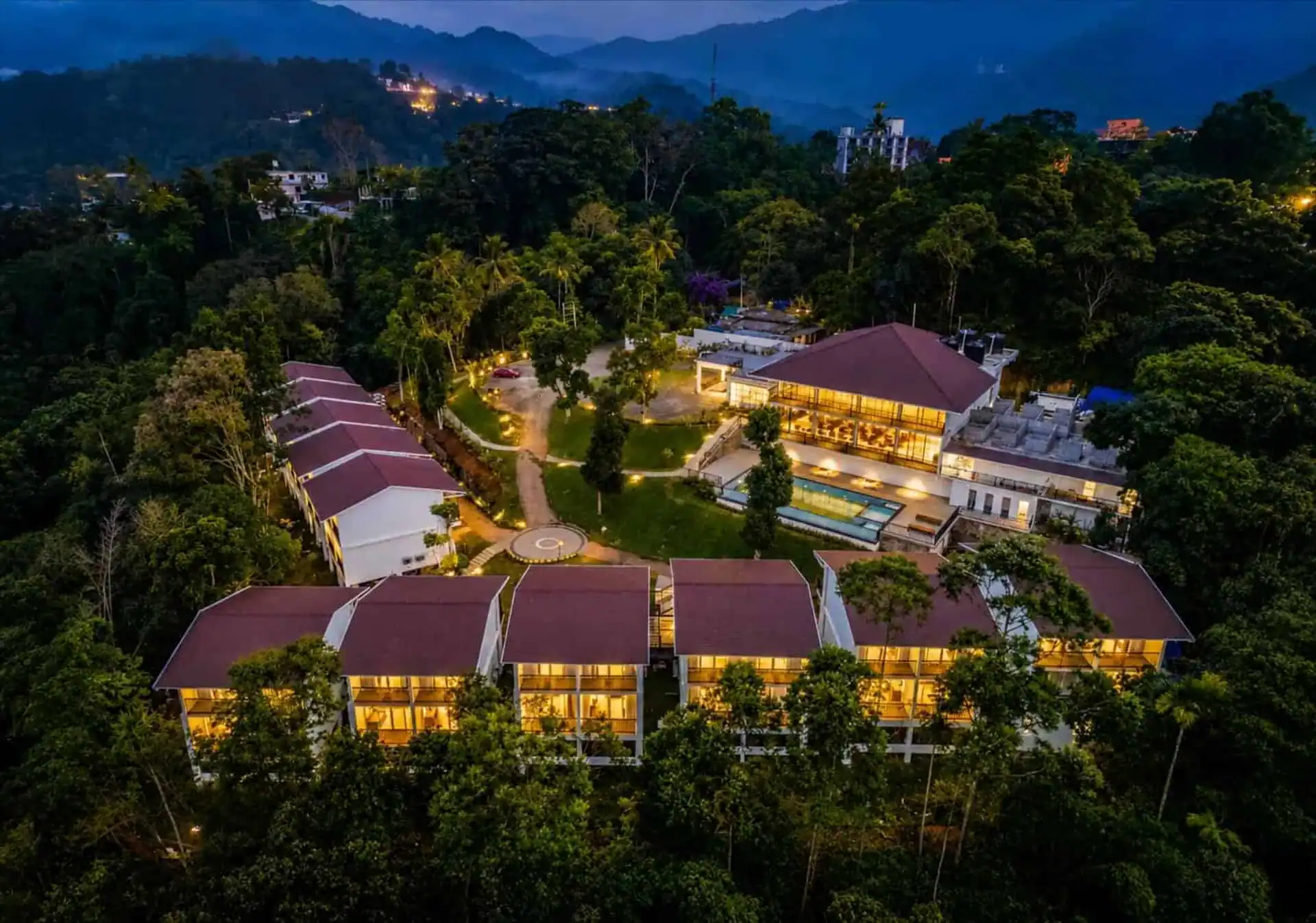 Vega Munnar Resort fully illuminated at blue-hour twilight with warm amber lights and forested valley beyond
