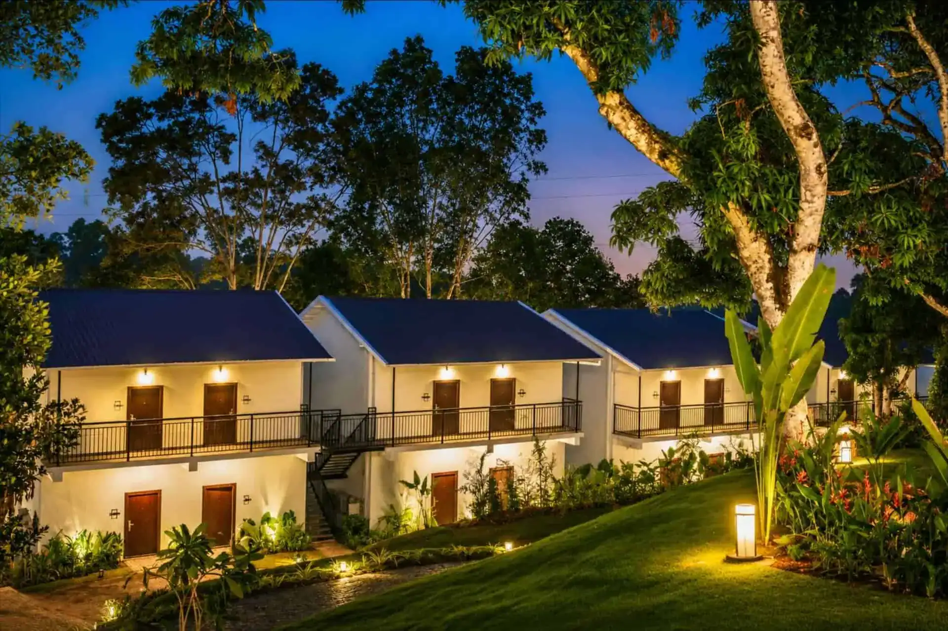 Cottage block at night with warm wall lanterns and banana plant garden