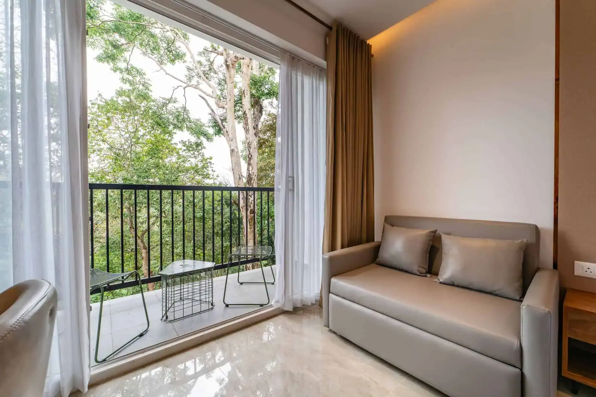 Grey sofa and sliding balcony door with eucalyptus canopy view in Vega Bliss Cottage